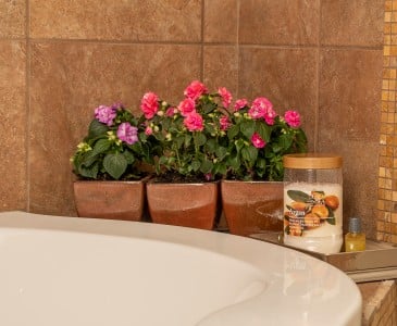 Mini-roses in copper pots sit on the ledge of a soaking tub.