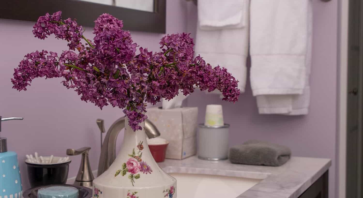 Bouquet of violet lilacs in a ceramic vase on a bathroom vanity. 