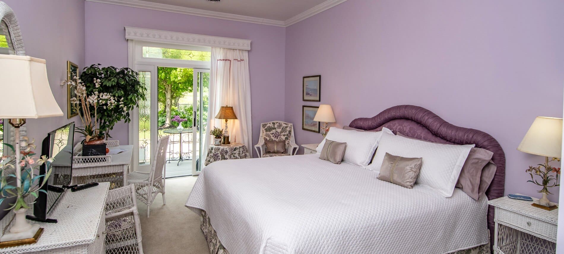 Light filled bedroom with lavender walls and a french door holds a bed with a purple upholstered headboard.