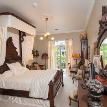 Elegant ivory bedroom holds large antique bed with an antique draped headboard.